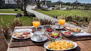 An outdoor breakfast setting with a table set with various breakfast items, including toast, eggs, and fruits, overlooking a garden and pool area. - Monte do Cardal (Aljezur)