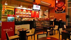 A Terra Bistro restaurant interior with a brick wall, a display case of food items, and several tables and chairs. - Platinum Suites (Dhaka)