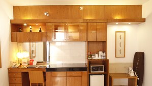 A compact kitchen with wooden cabinets, a refrigerator, a microwave, and a small ironing board. - Platinum Suites (Dhaka)
