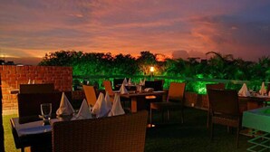An outdoor restaurant with tables and chairs, surrounded by greenery and a brick wall. - Platinum Suites (Dhaka)