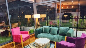 Ein modernes Wohnzimmer mit einem grünen Sofa, einem pinken Sessel und einem violetten Sessel. In der Mitte steht ein runder Couchtisch.