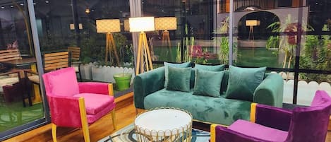 Una sala de estar moderna con un sofá verde, una butaca rosa y una butaca morada. En el centro, hay una mesa de centro redonda.