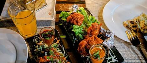 Une table à manger dressée avec différents plats, notamment du poulet frit, du riz et une salade, ainsi que des boissons et une lanterne décorative.
