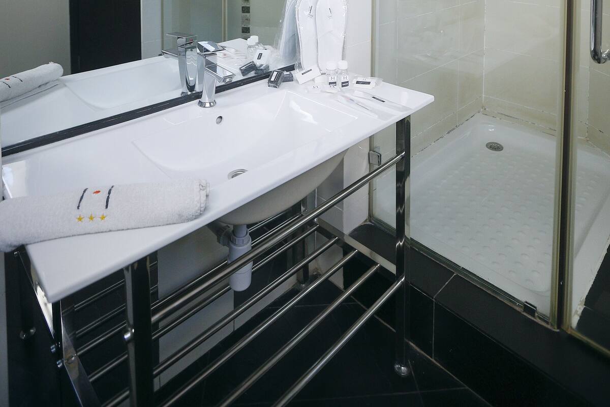 Une salle de bain moderne avec un grand miroir, un lavabo blanc et une douche à parois de verre.