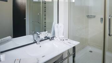 Un baño moderno con un espejo grande, un lavabo blanco y una ducha con mampara de vidrio.