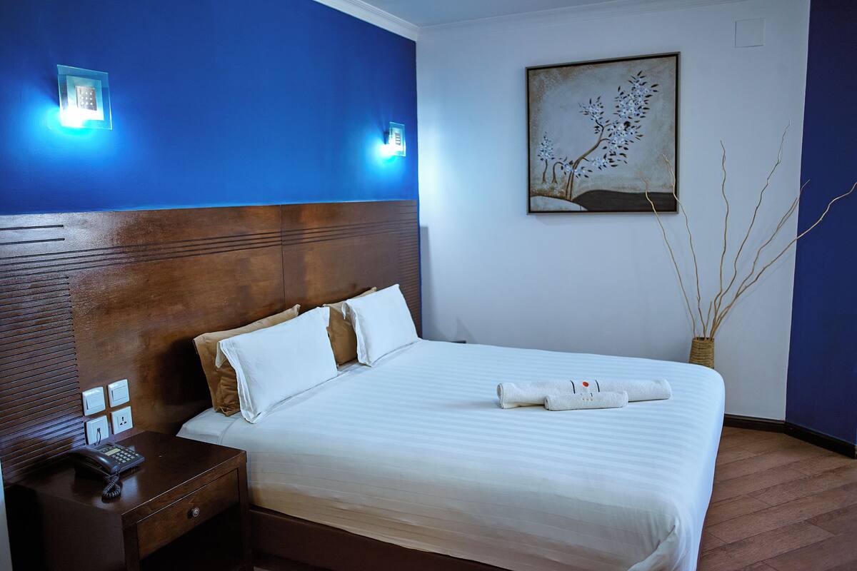 Une chambre d’hôtel avec un grand lit, une tête de lit en bois, une table de chevet avec un téléphone et un tableau au mur.