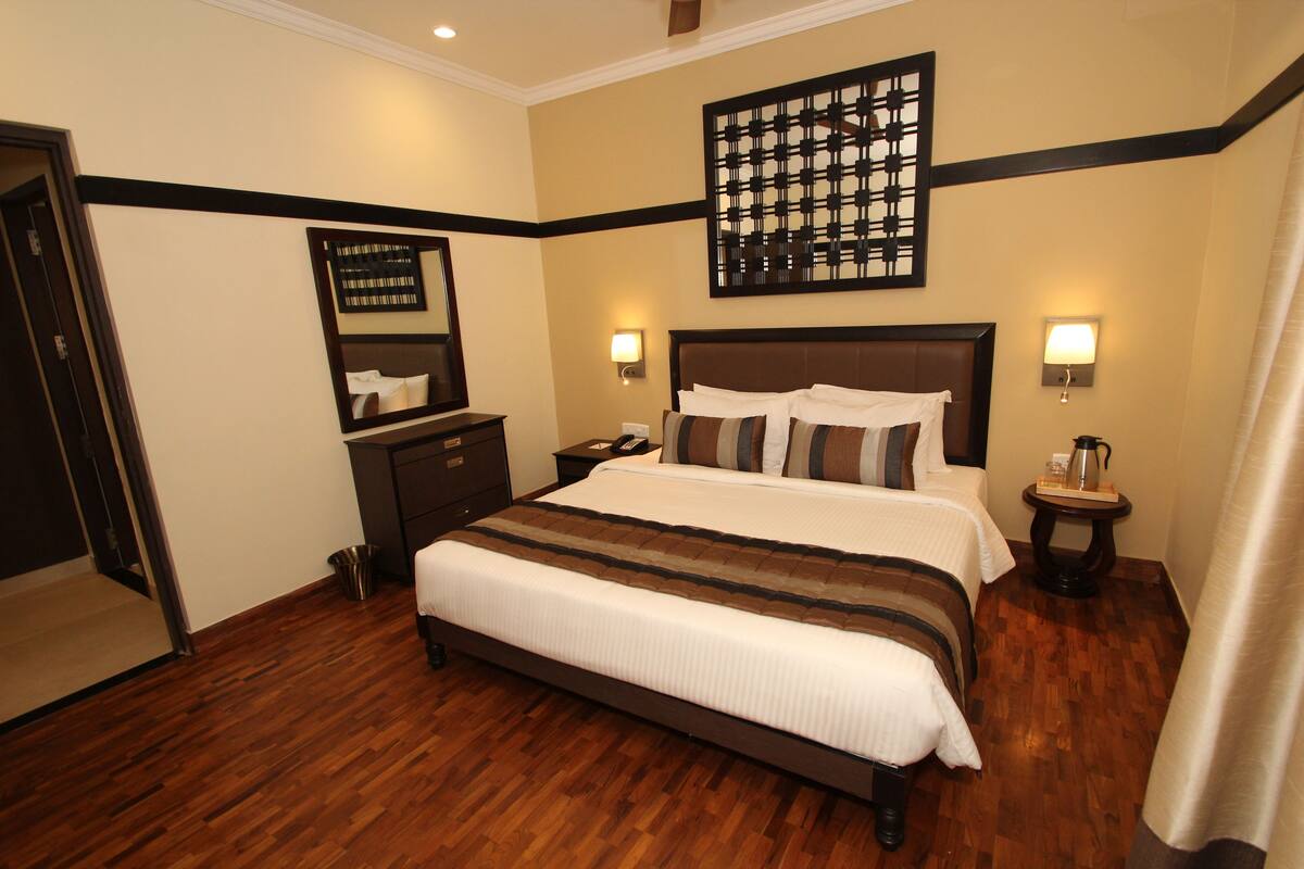 A hotel room with a large bed, a nightstand, a wall-mounted clock, and a framed picture.