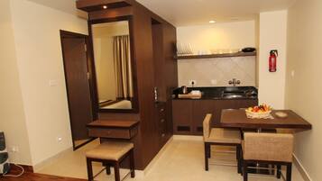 A compact hotel room with a kitchenette, a dining area with a table and chairs, a large mirror, and a radiator.