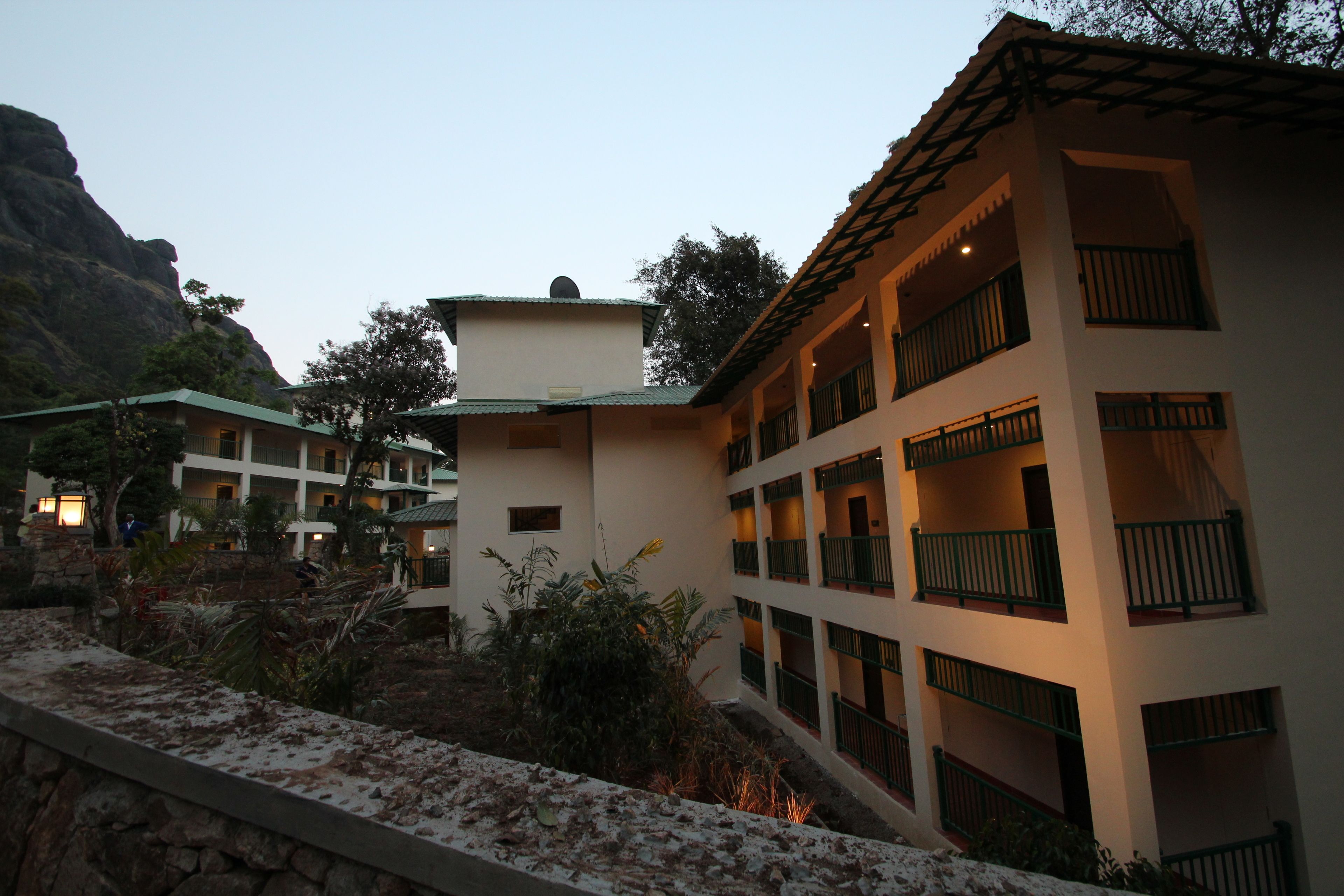 A multi-story hotel with balconies, a stone retaining wall, and a mountainous backdrop.