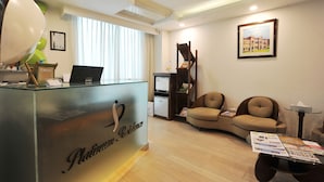 A reception area with a reception desk, a computer, a seating area with two sofas, a small table with brochures, and a framed picture on the wall.