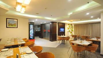 A modern dining area with tables set for guests, a television screen, and a view of the restaurant's interior.