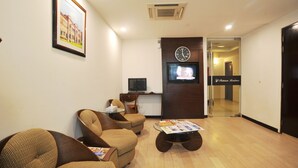 A reception area with a wooden floor, a sofa, a coffee table, a TV, and a clock on the wall.