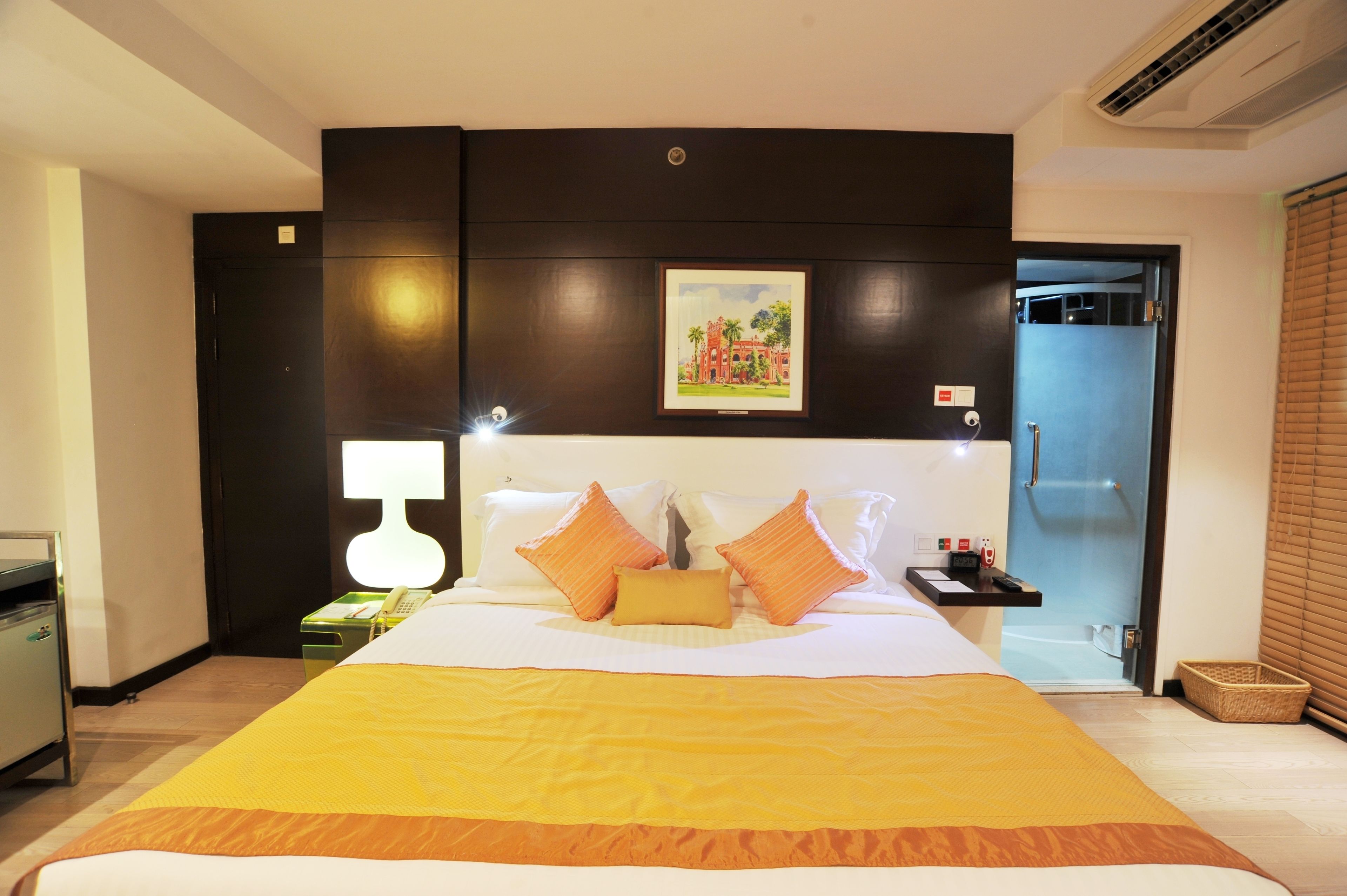Habitación de hotel con cama, mesita de noche, lámpara, un cuadro en la pared y puerta de baño.