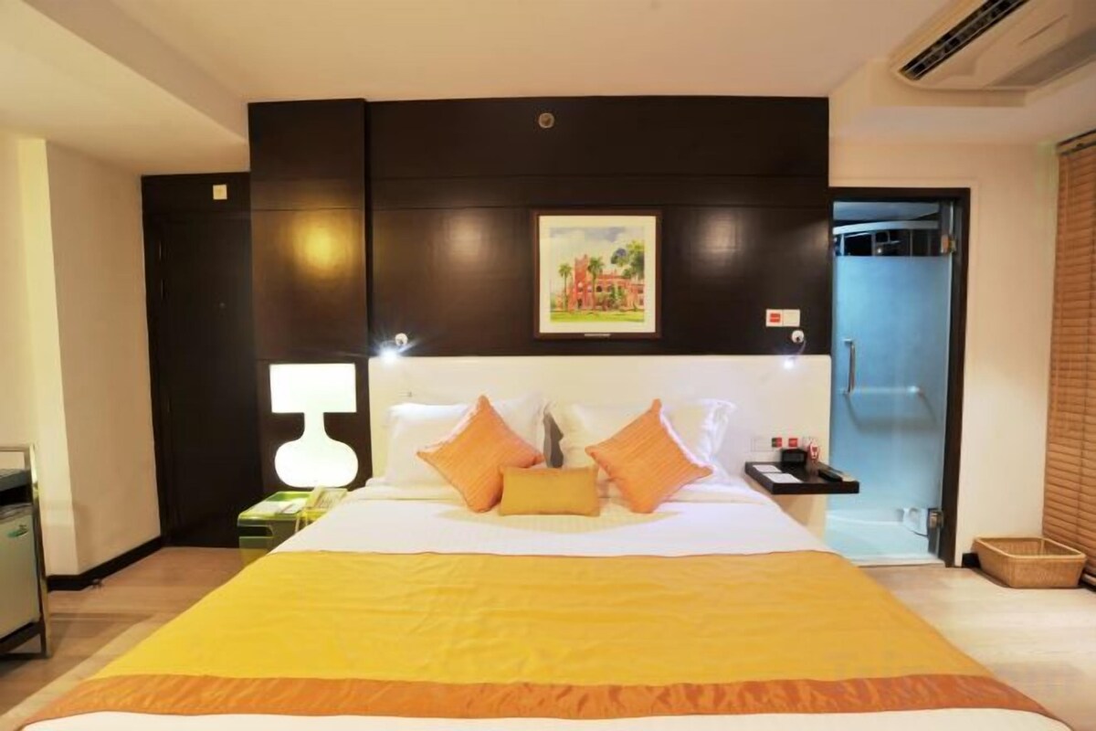 A hotel room with a large bed, a bedside table with a lamp, a painting on the wall, and a bathroom door.