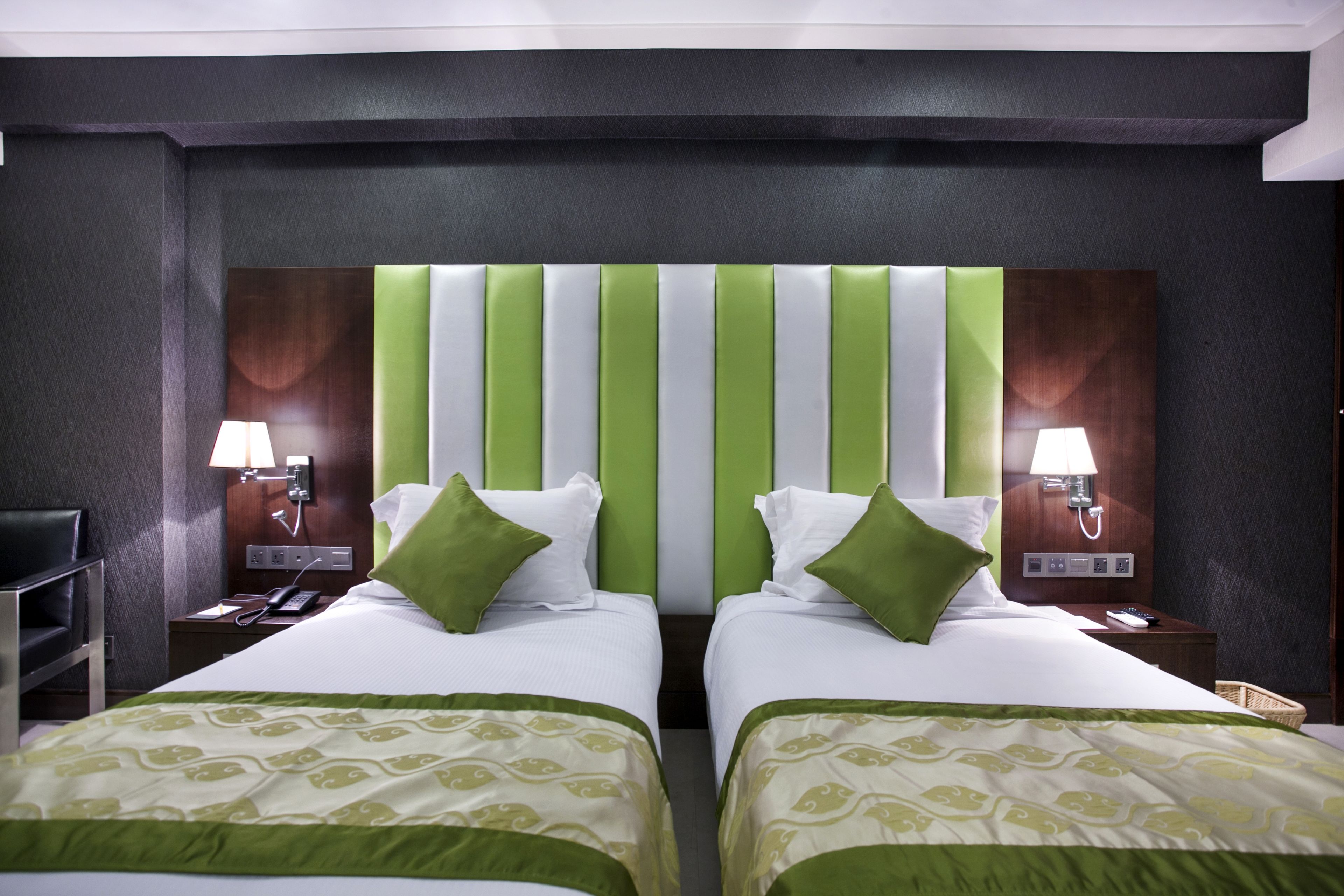 A hotel room with two beds, green and white striped headboards, and bedside lamps.
