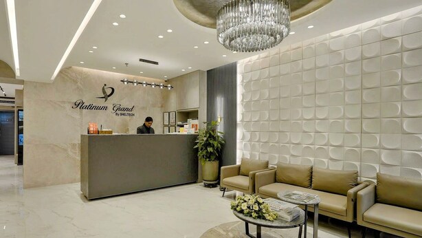 A reception area with a marble counter, a chandelier, a sofa, and a coffee table. - Platinum Grand (Dhaka)