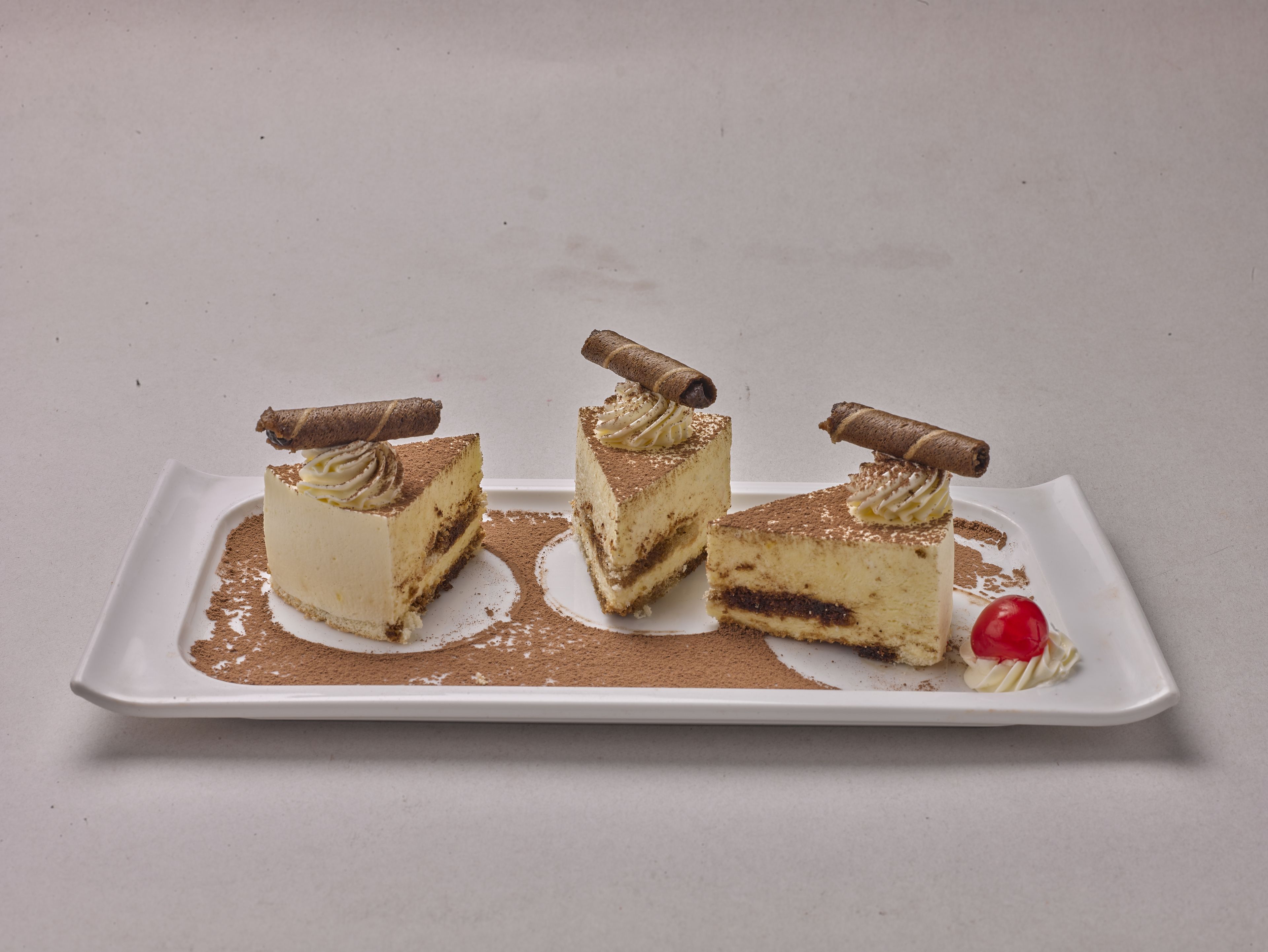 Tres rebanadas de pastel en capas con cobertura de chocolate y crema sobre un plato blanco.