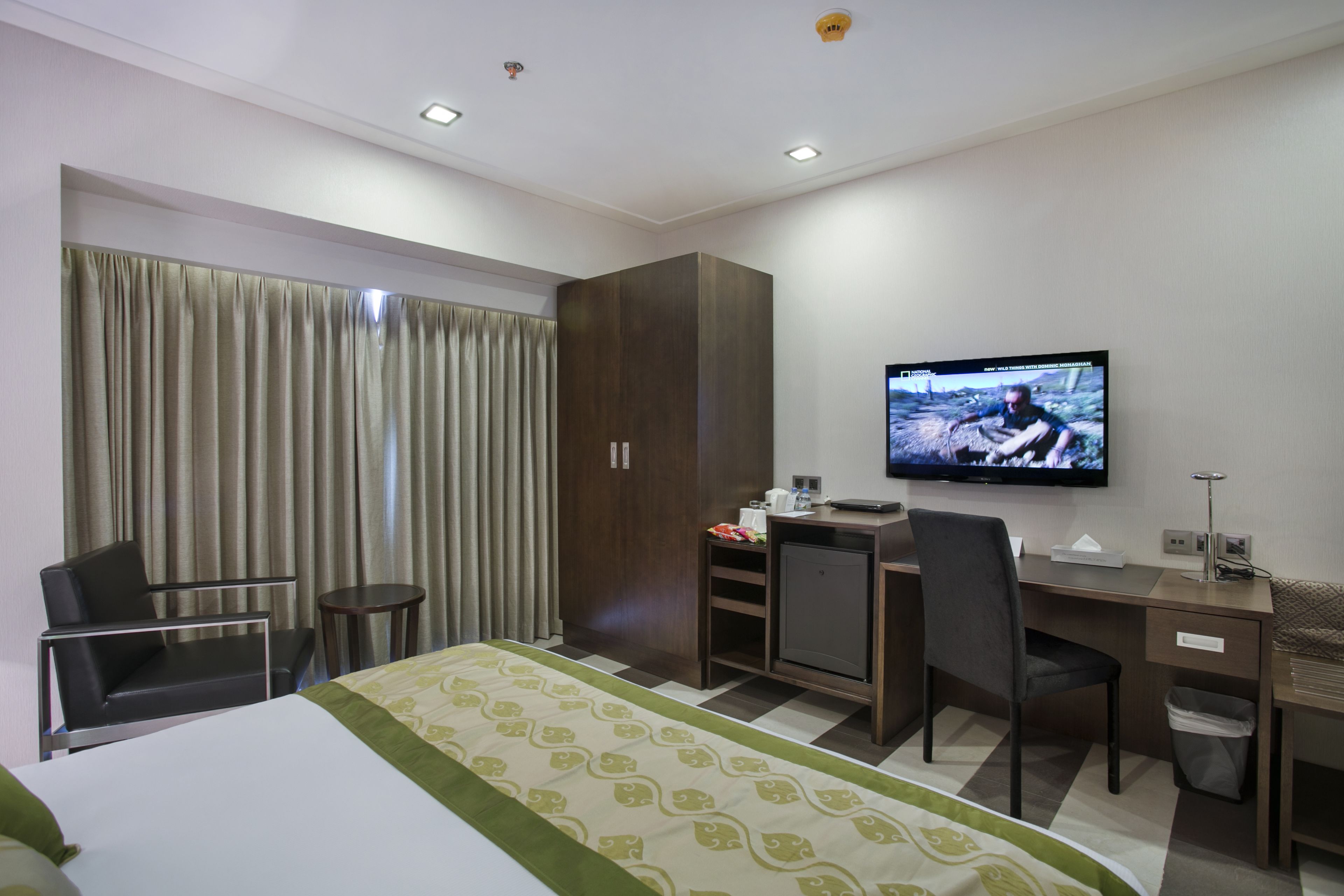 Habitación de hotel con cama, escritorio, silla, televisión y armario.