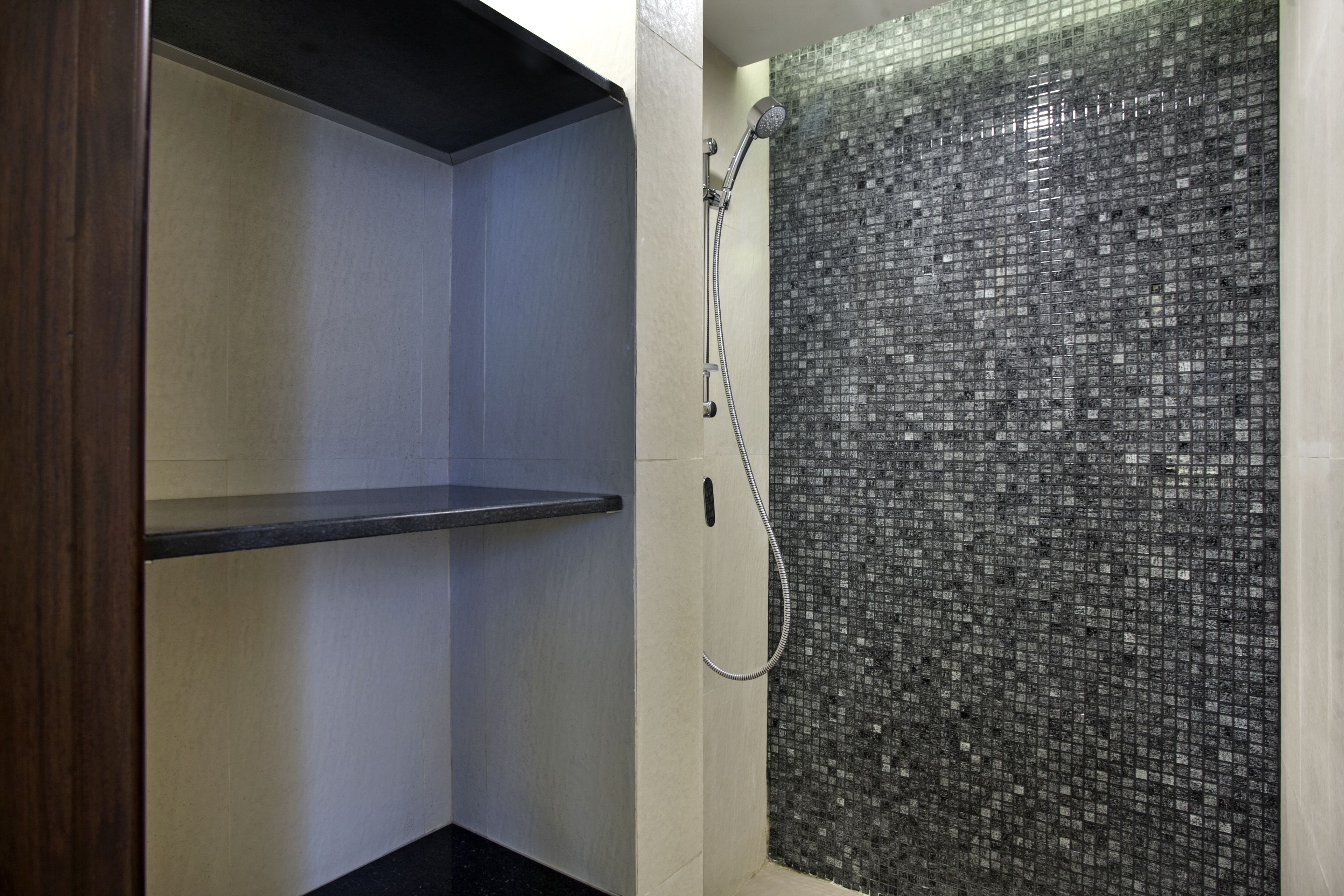 A shower with a mosaic tile wall, a wooden shelf, and a metal showerhead.