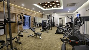 A modern gym with various exercise equipment, a wooden wall, and a ceiling with recessed lighting. - Platinum Grand (Dhaka)