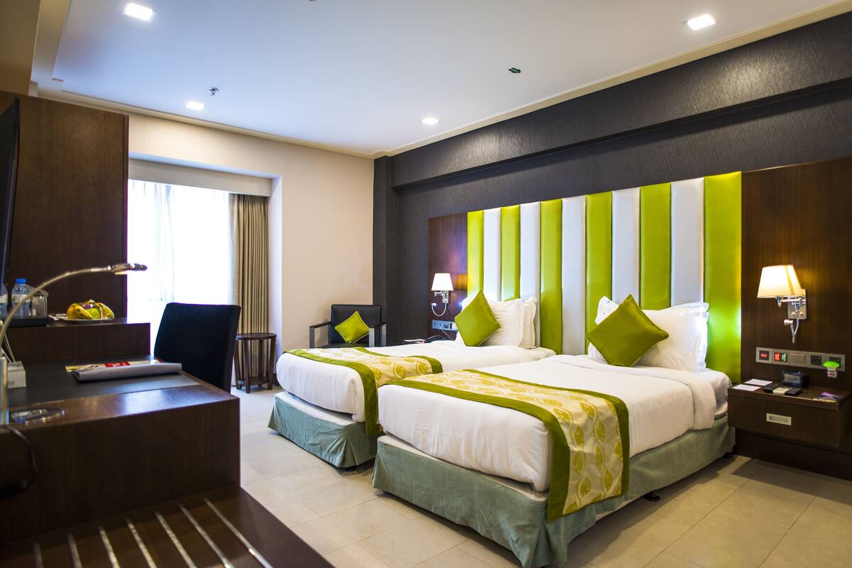 Une chambre d’hôtel avec deux lits, un bureau, une chaise et une table de chevet avec une lampe.