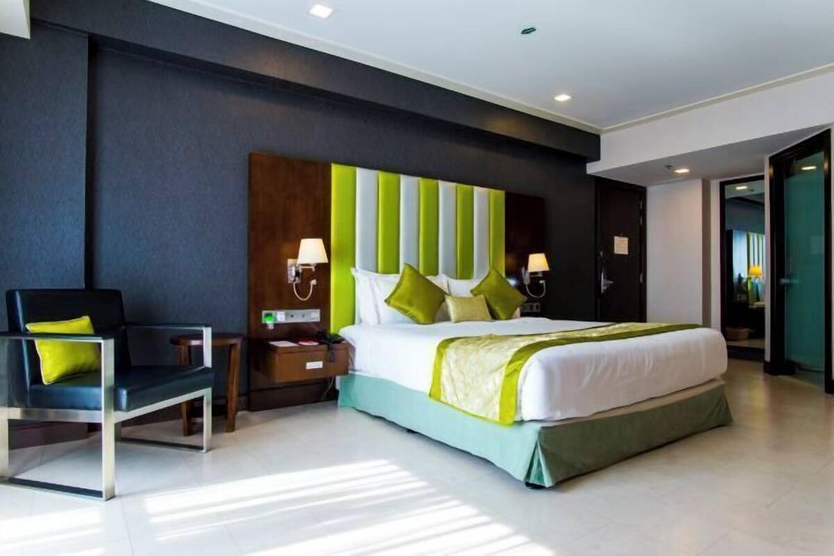Une chambre d’hôtel moderne avec un grand lit, une chaise, des tables de chevet et une tête de lit à rayures originale.