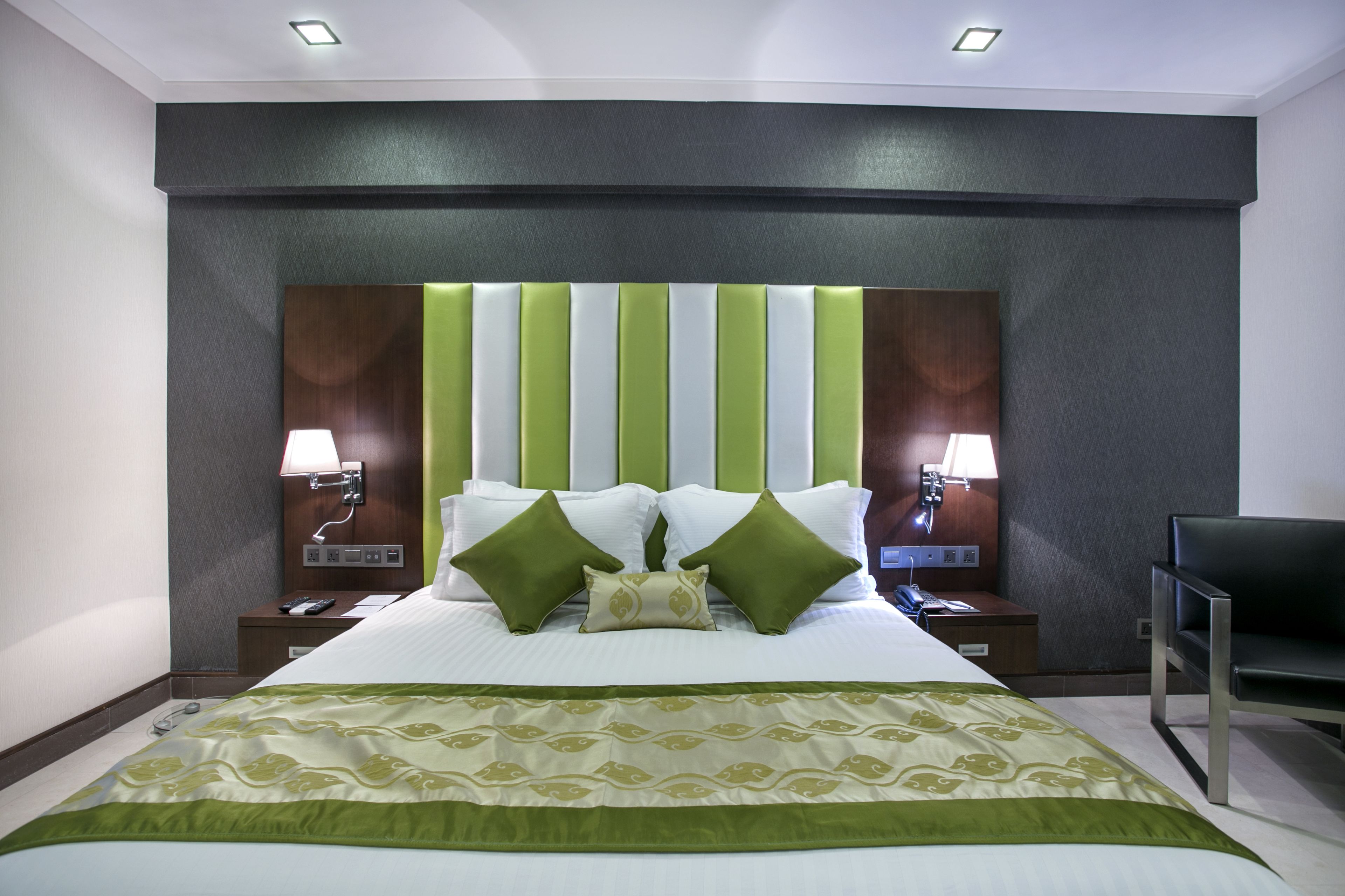 A hotel room with a large bed, green and white striped headboard, two bedside lamps, and a chair.