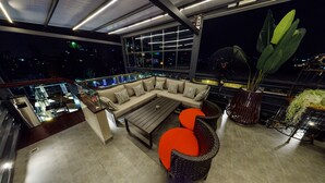 A modern rooftop lounge with a sofa set, a coffee table, and wicker chairs. - Platinum Grand (Dhaka)