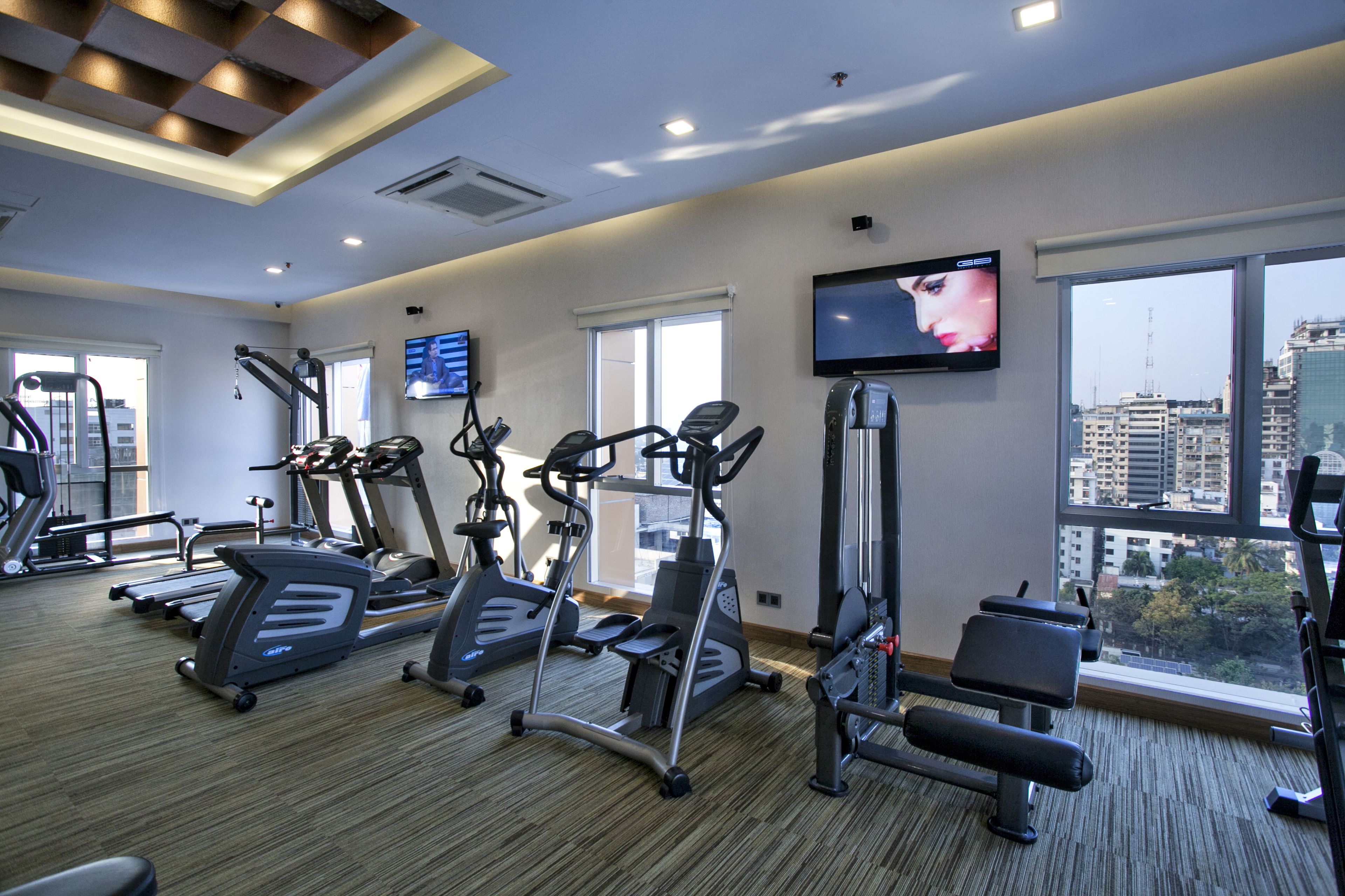 A gym with treadmills, elliptical machines, and a TV on the wall.