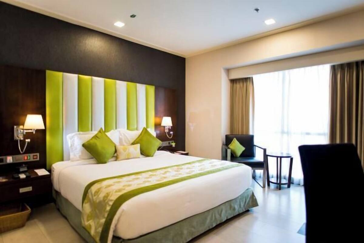 Une chambre d’hôtel avec un grand lit, deux tables de chevet, une chaise et une fenêtre avec des rideaux.