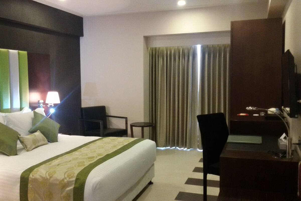 Une chambre d’hôtel avec un grand lit, un bureau, une chaise, une télévision et des rideaux.