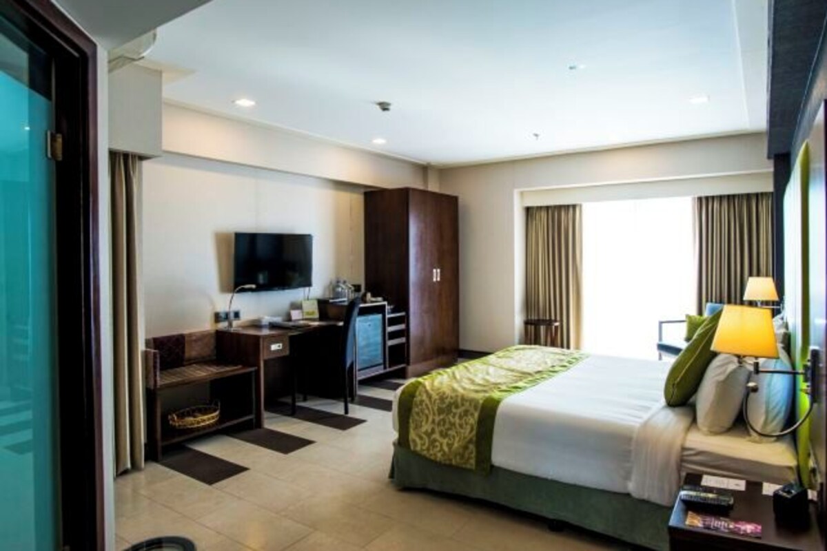 Una habitación de hotel con cama, escritorio, silla, televisión y ventana con cortinas.