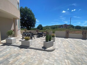 An outdoor patio with tables and chairs, surrounded by planters and a view of a hillside.