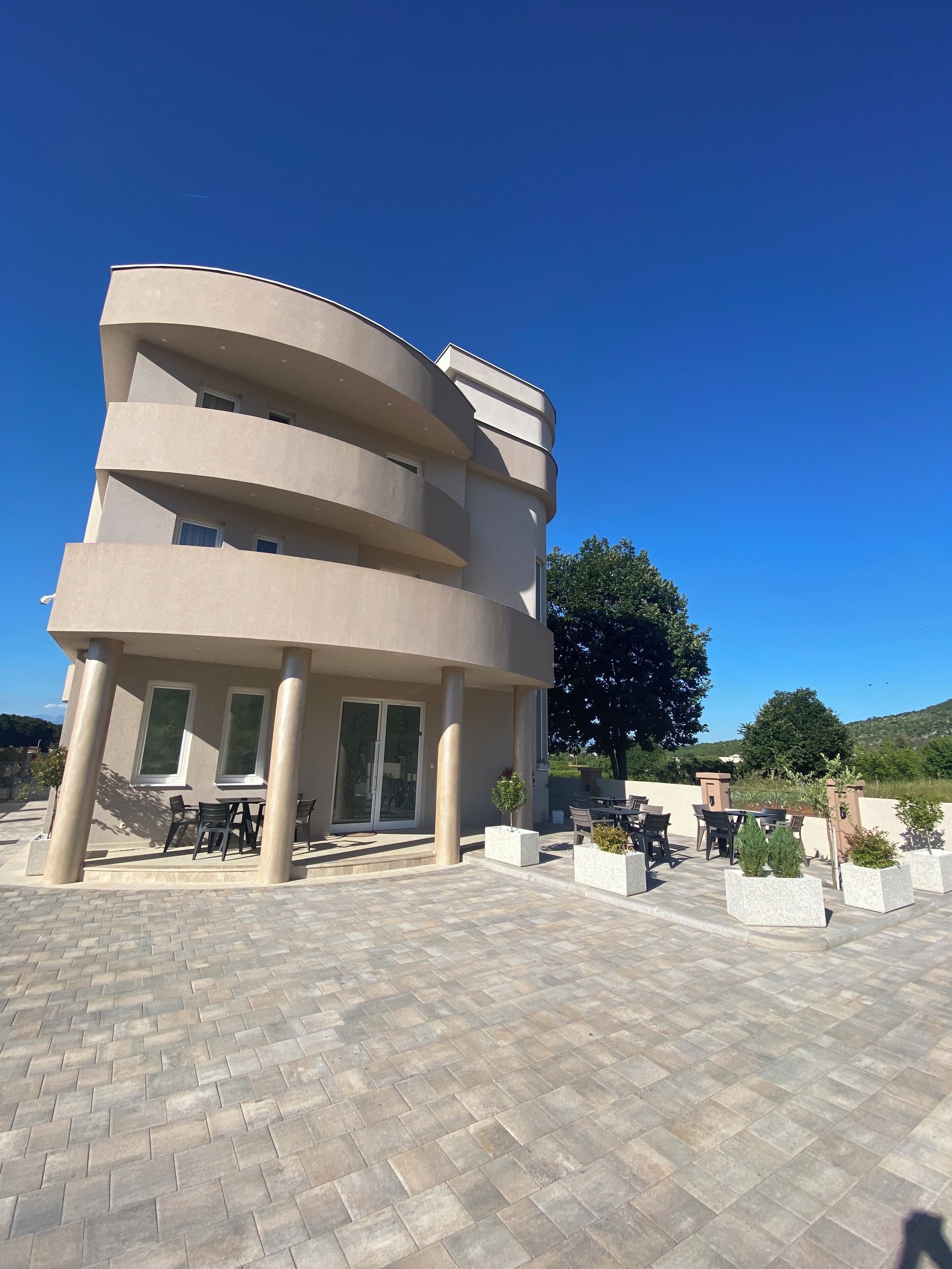 Ein modernes Gebäude mit einer gewölbten Fassade, mehreren Balkonen und Außenbereichen mit Pflanzkübeln.