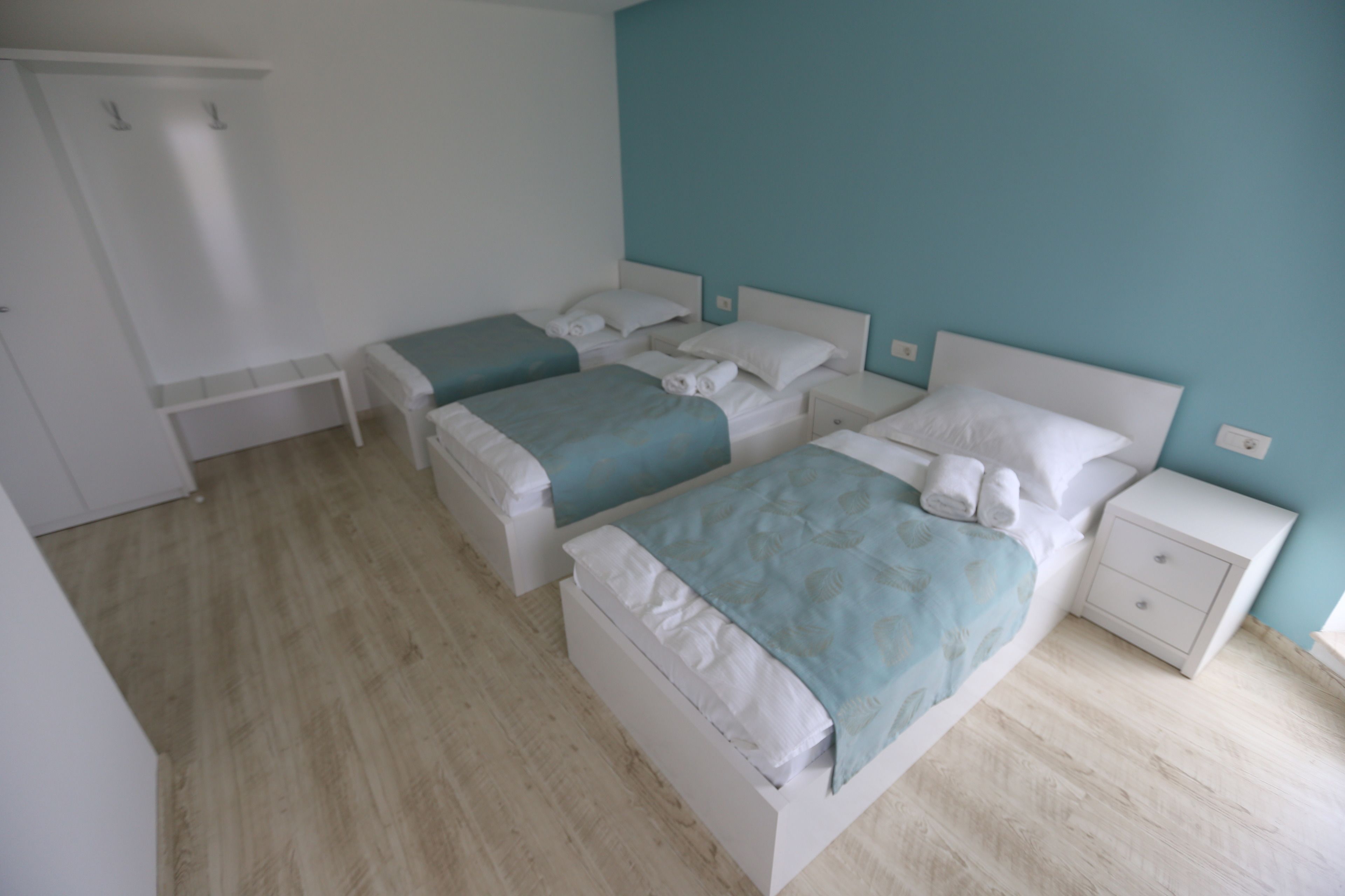 Ein Schlafzimmer mit drei Betten, einem weißen Kleiderschrank und einer kleinen Bank.
