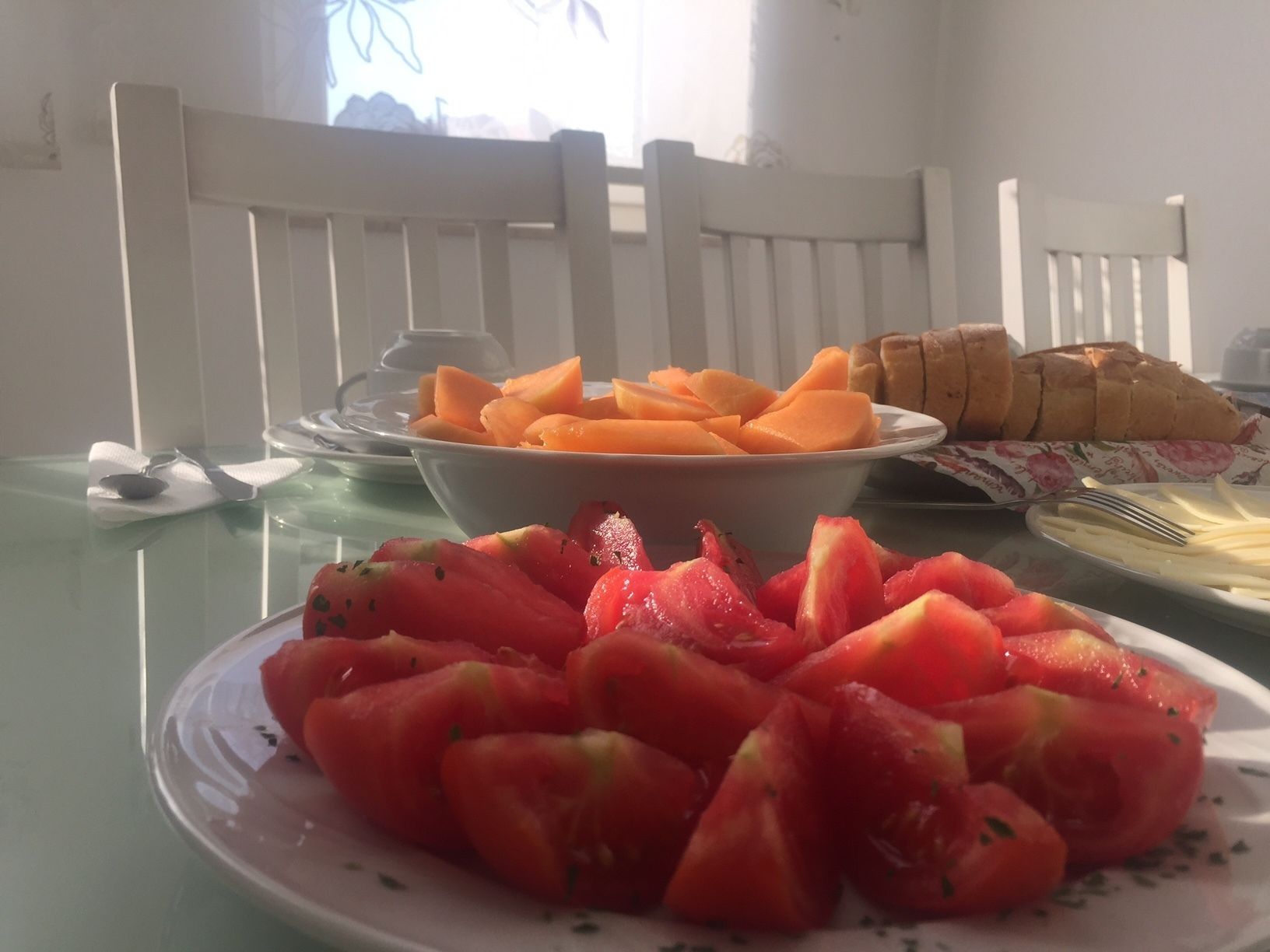 A breakfast table with a plate of sliced strawberries, a bowl of cantaloupe, and a basket of bread.