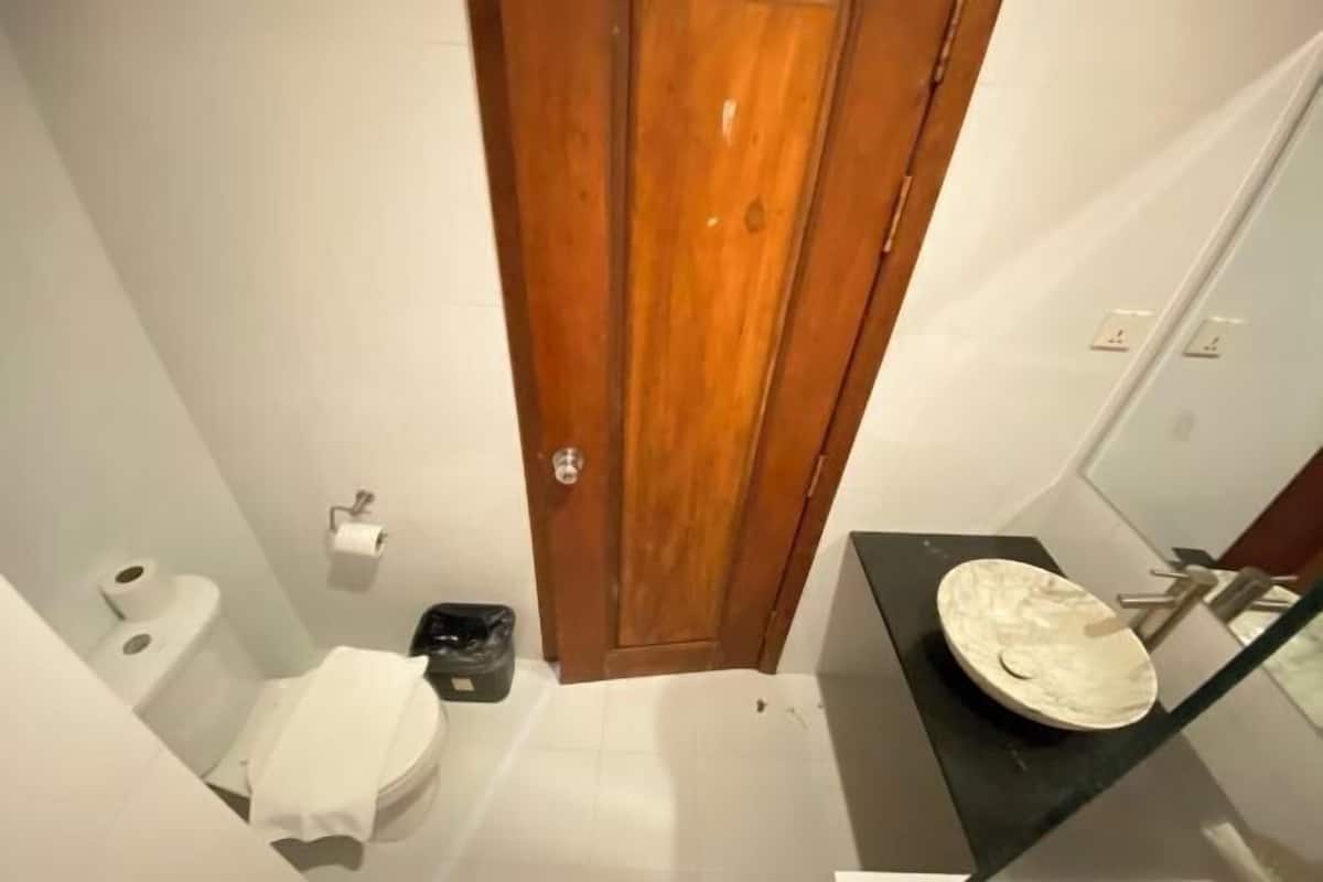 Un baño con inodoro, lavamanos, puerta y un cubo de basura.