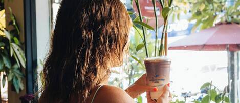 Una persona sentada a una mesa con una bebida, frente a un ventanal con un letrero que dice 'Coffee'.