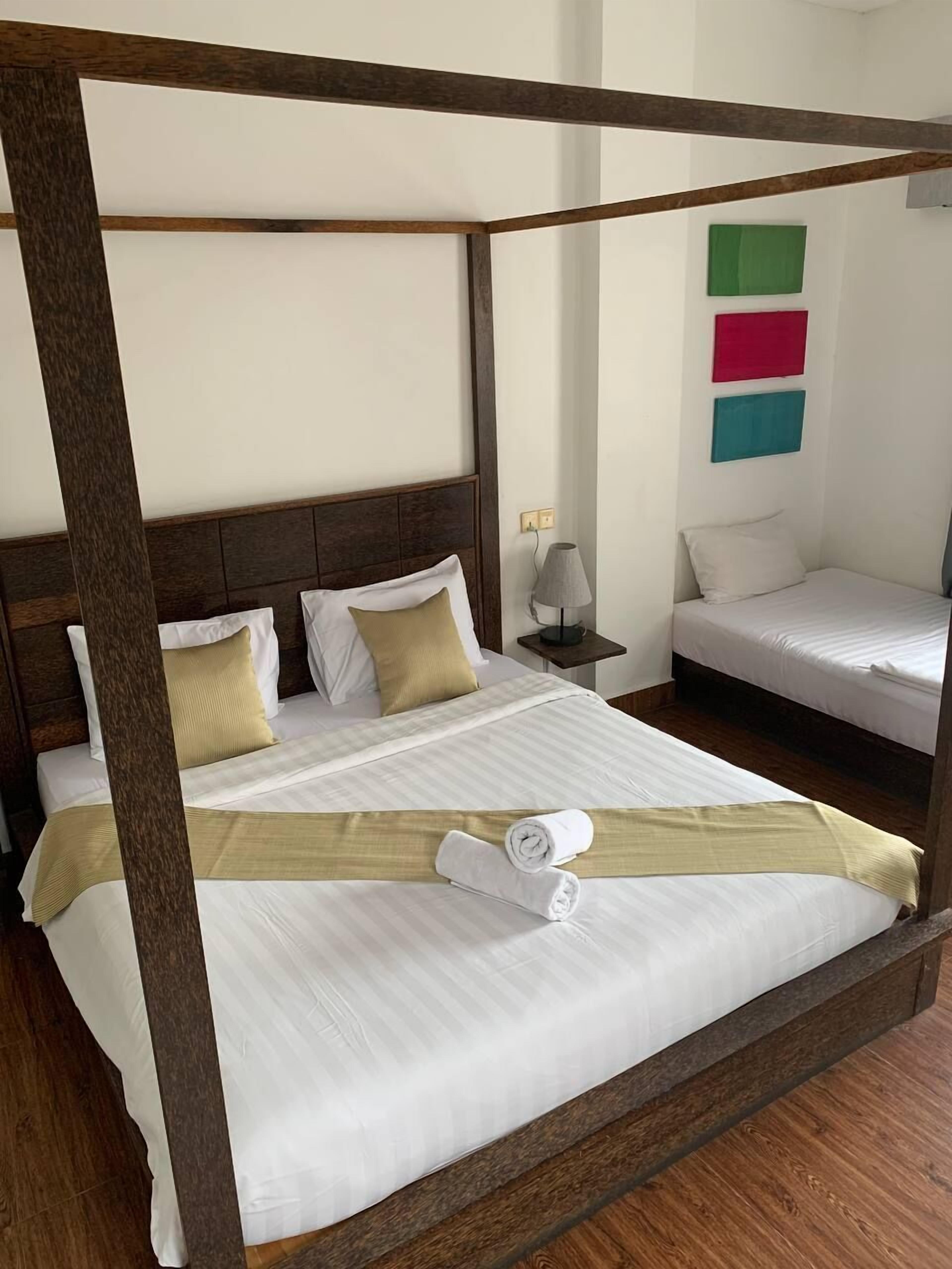 A four-poster bed with white bedding and a beige throw, a bedside table with a lamp, and a small bedside table with a lamp.