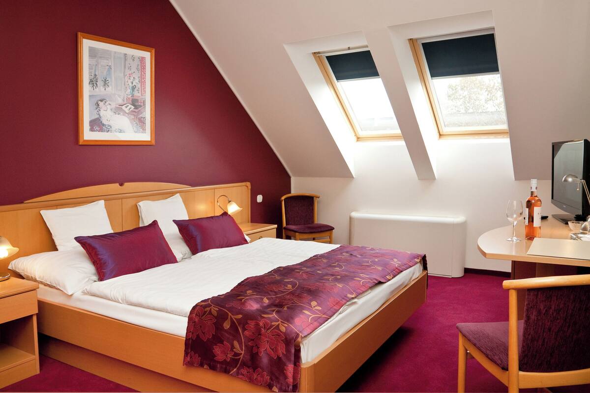 Un dormitorio con cama, escritorio, silla, televisor y dos ventanas.