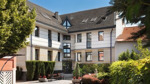 A courtyard with a building featuring a tiled roof, multiple windows, and a small garden area with benches and potted plants. - Hotel Kálvária (Gyor)