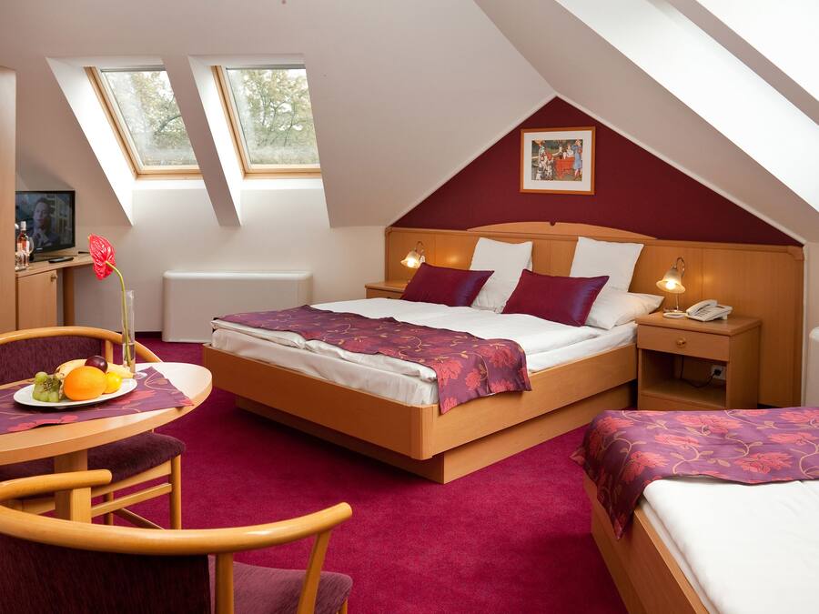 Un dormitorio con cama, escritorio y silla. Hay dos ventanas y un cuadro en la pared.