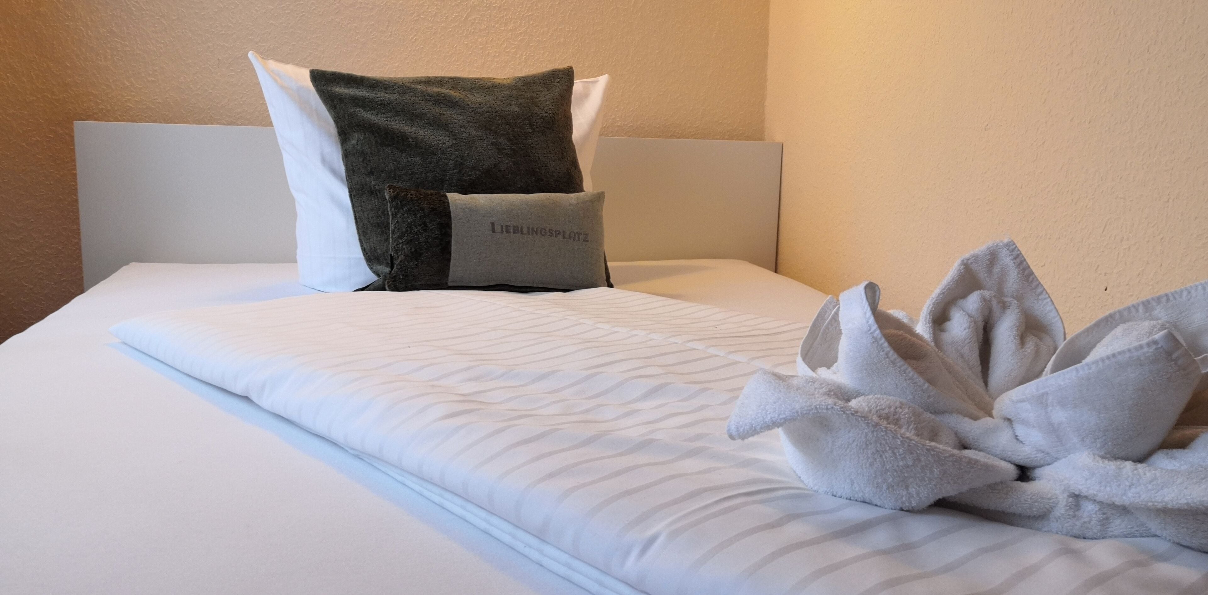 A neatly made bed with a white comforter, two pillows, and a towel arrangement.