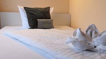 A neatly made bed with a white comforter, two pillows, and a towel arrangement.