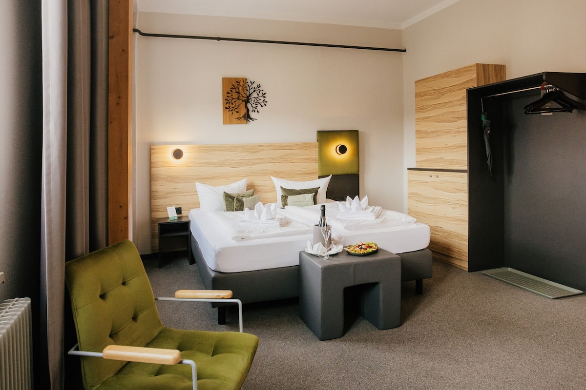 A hotel room with a bed, a chair, a bedside table, a wall-mounted artwork, and a coat rack.