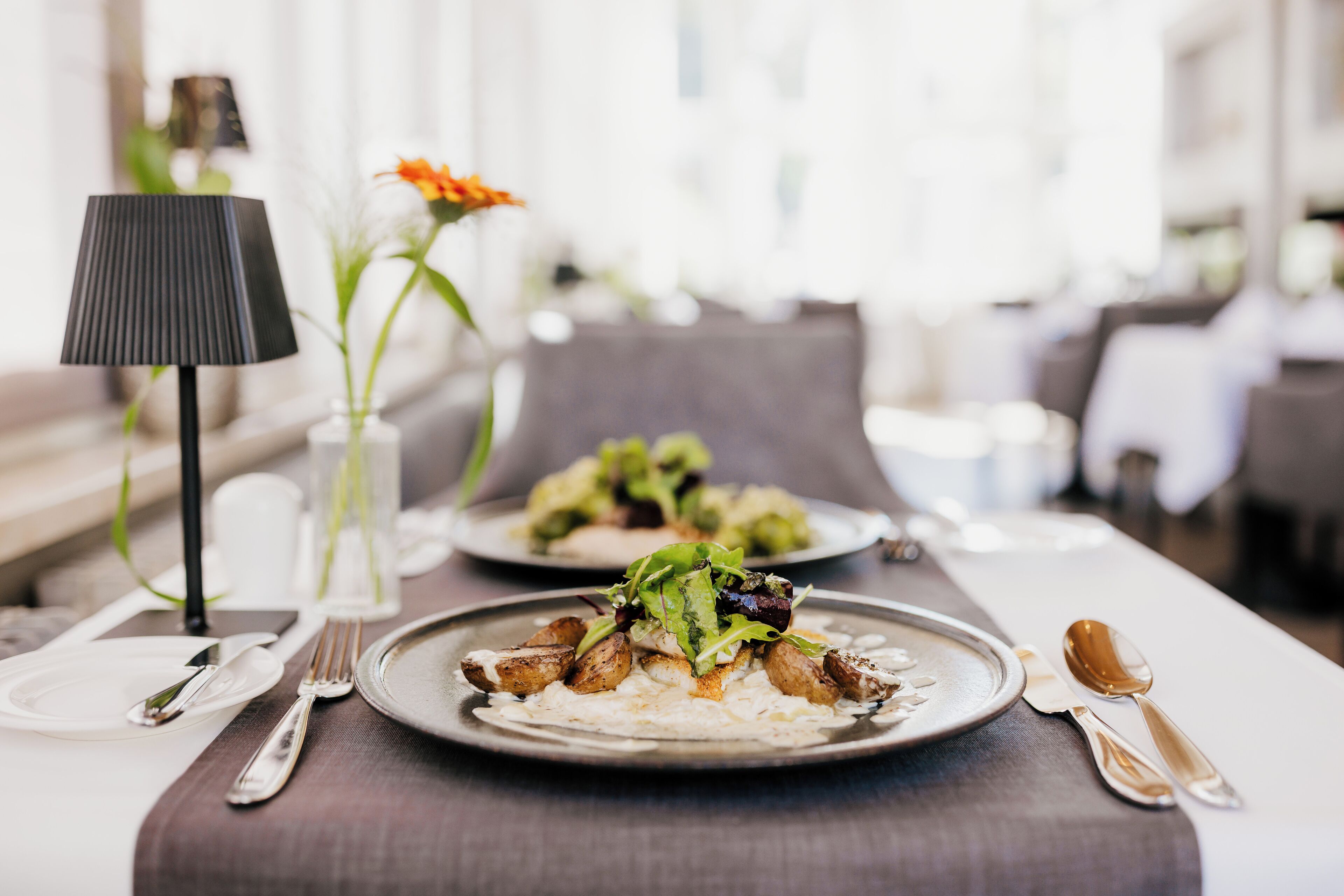A dining table set with plates of food, cutlery, and a lamp.