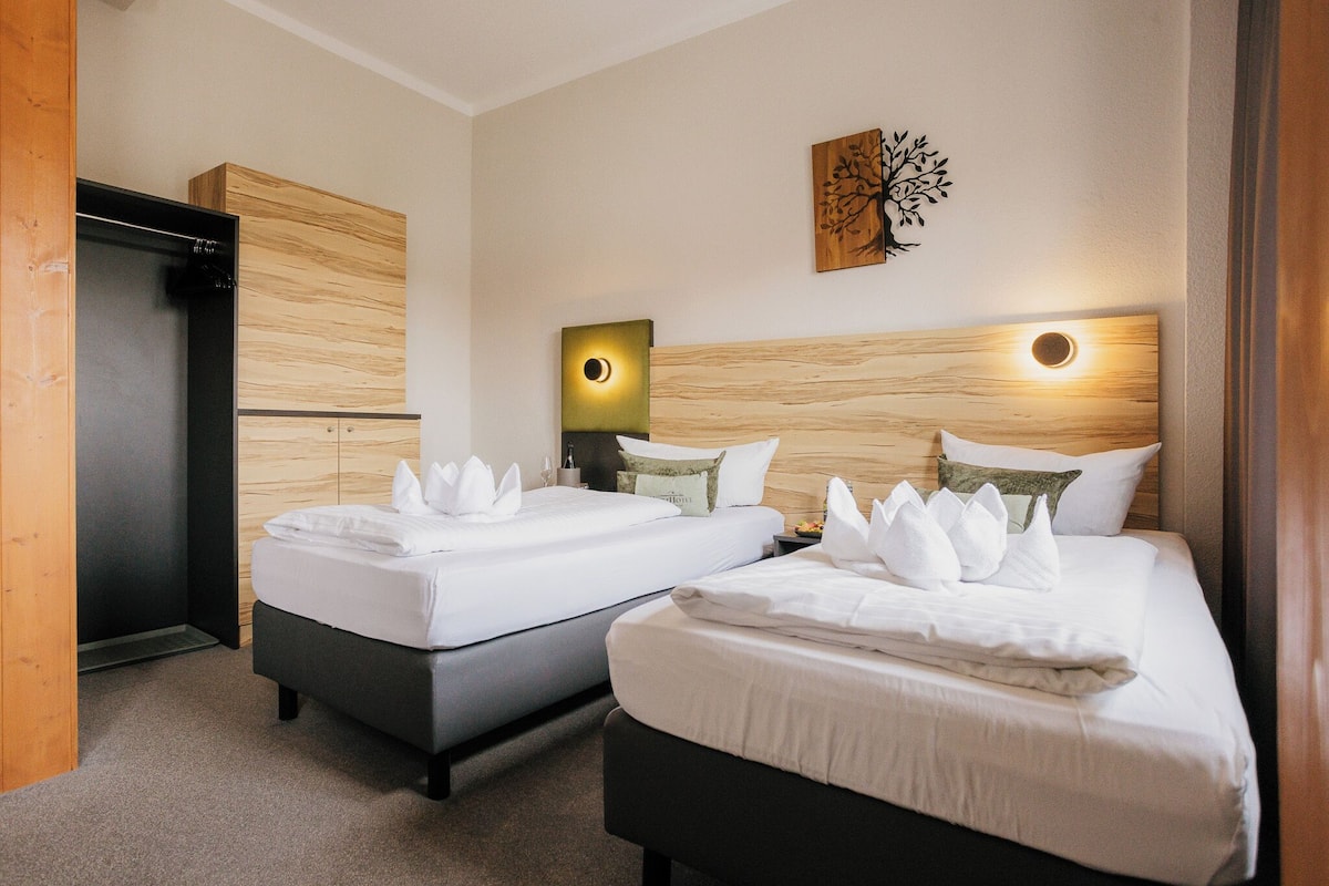 A hotel room with two beds, a wooden headboard, a wall-mounted artwork, and a nightstand with a lamp.