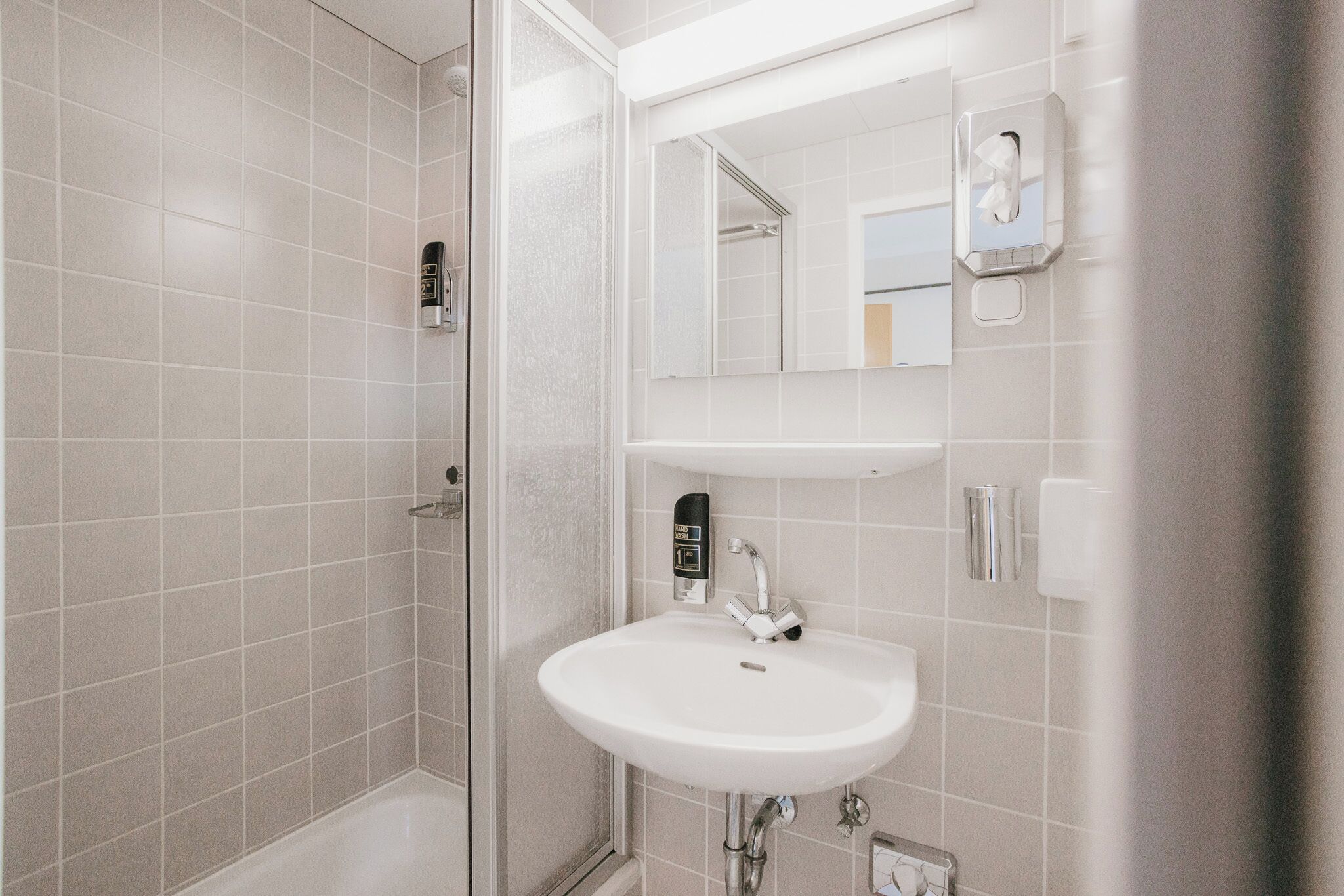 Een badkamer met een douchecabine van glas, een wit wastafelmeubel en een spiegel erboven.