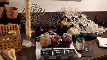 Una mesa de buffet con diversos alimentos y condimentos, incluyendo frascos de conservas y un pastel.