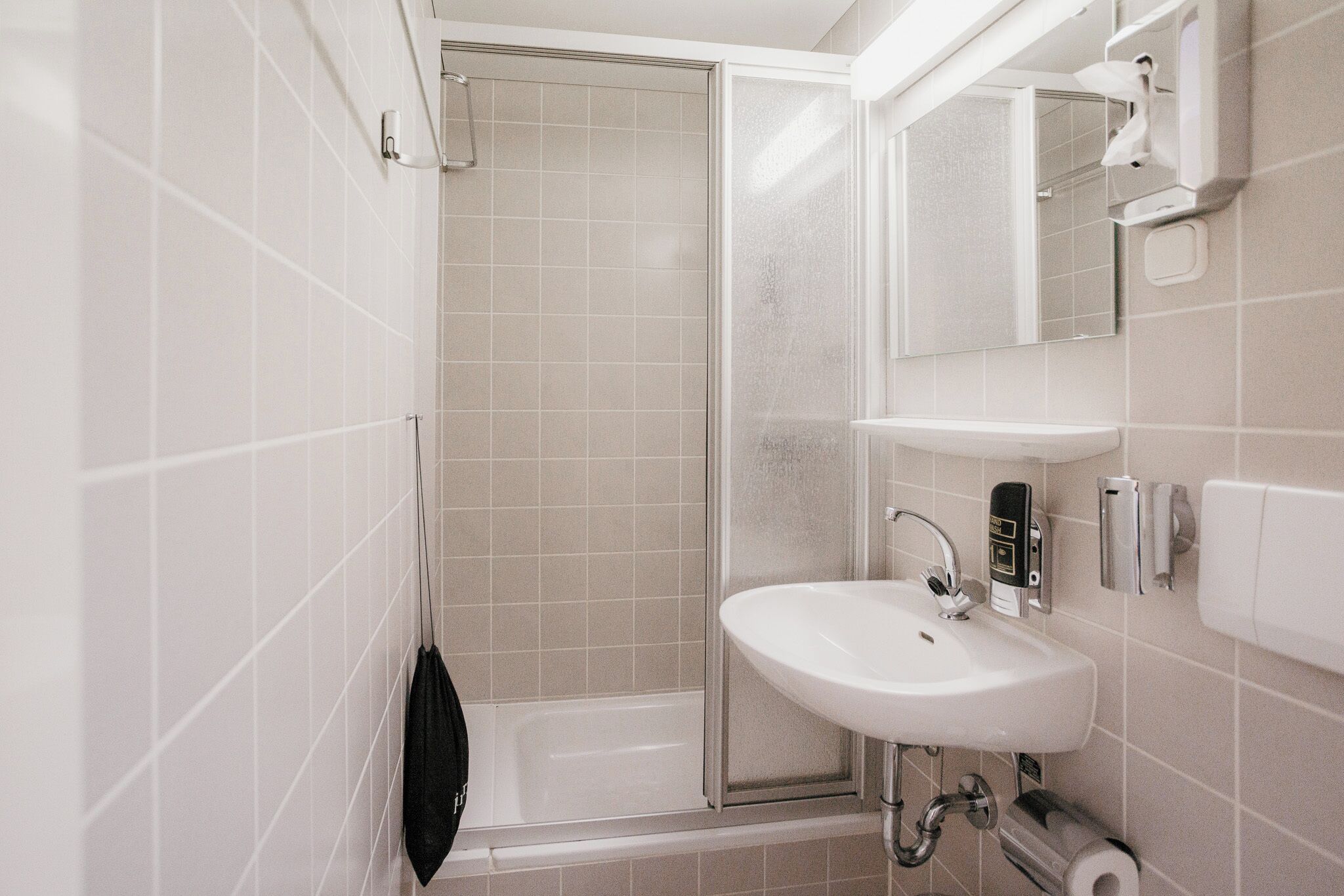 Ein Badezimmer mit weißem Waschbecken, einem Spiegel, einer Dusche und einer Toilette.